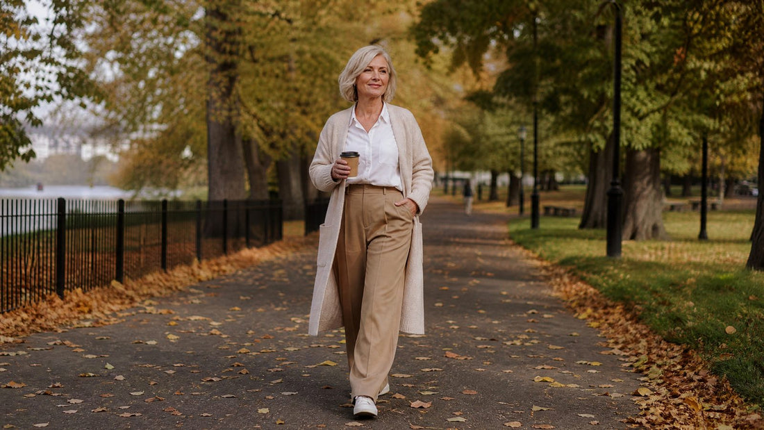 Woman in her early 50s walking in a park in autumn in high-waisted trousers and a tucked-in white shirt