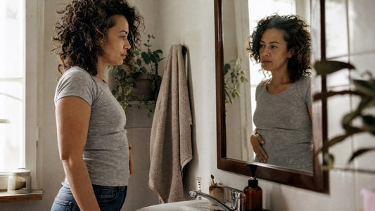 Woman in her 40s looking at her stomach in the bathroom mirror in the morning